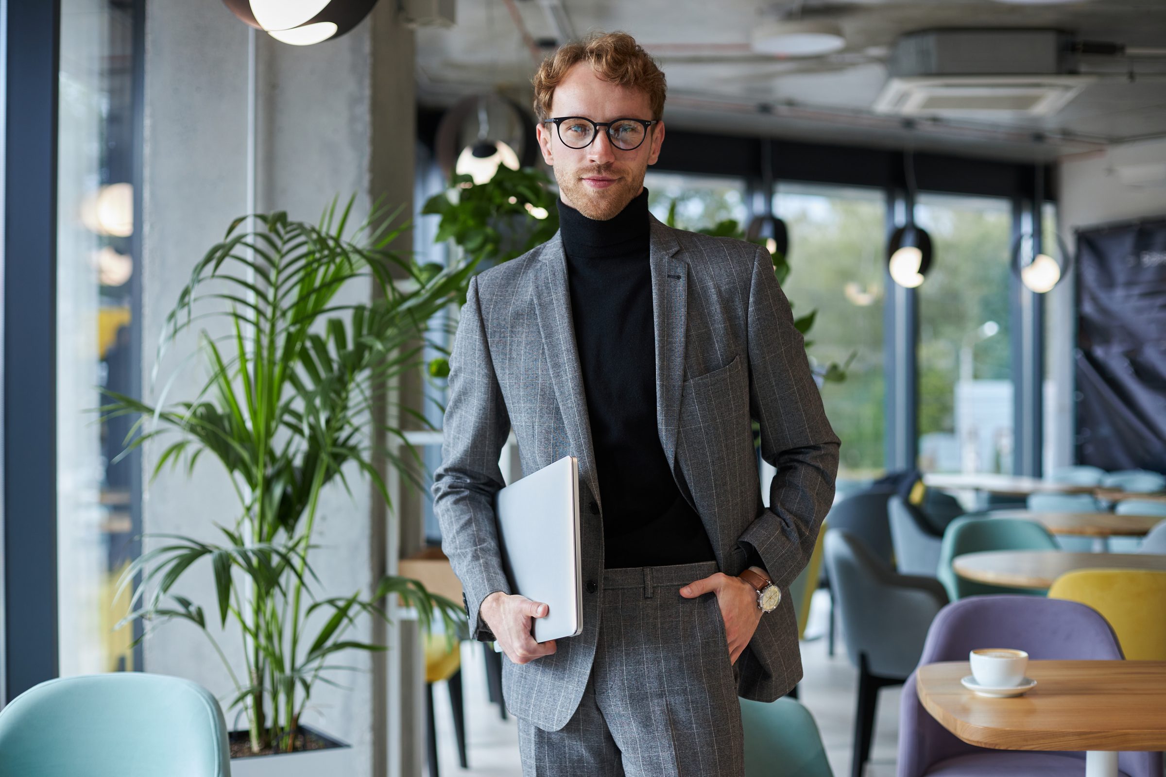 A man in a gray suit holding a laptop in a bright office